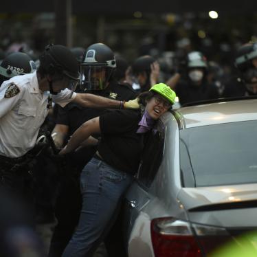 Police push a woman in a green hat against a car and handcuff her